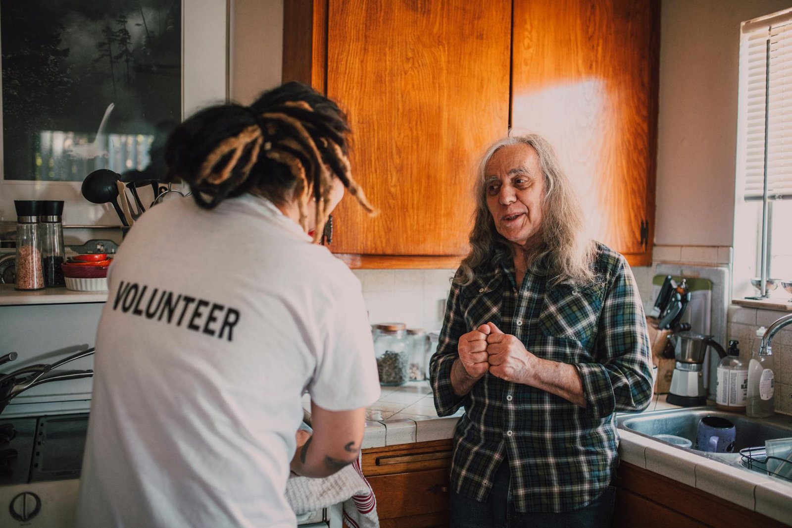 A volunteer helps a senior adult in a homely kitchen environment, showcasing community support and care.