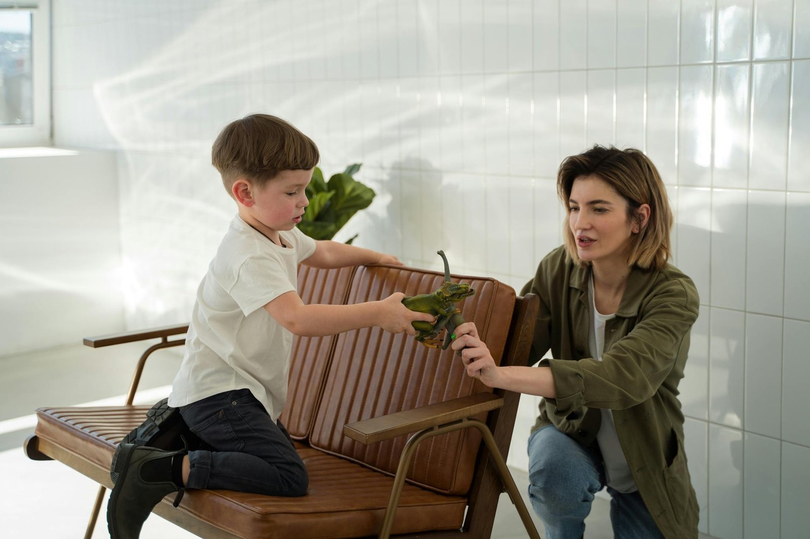 Mother and son enjoy quality time playing with toy dinosaurs in a sunlit room.