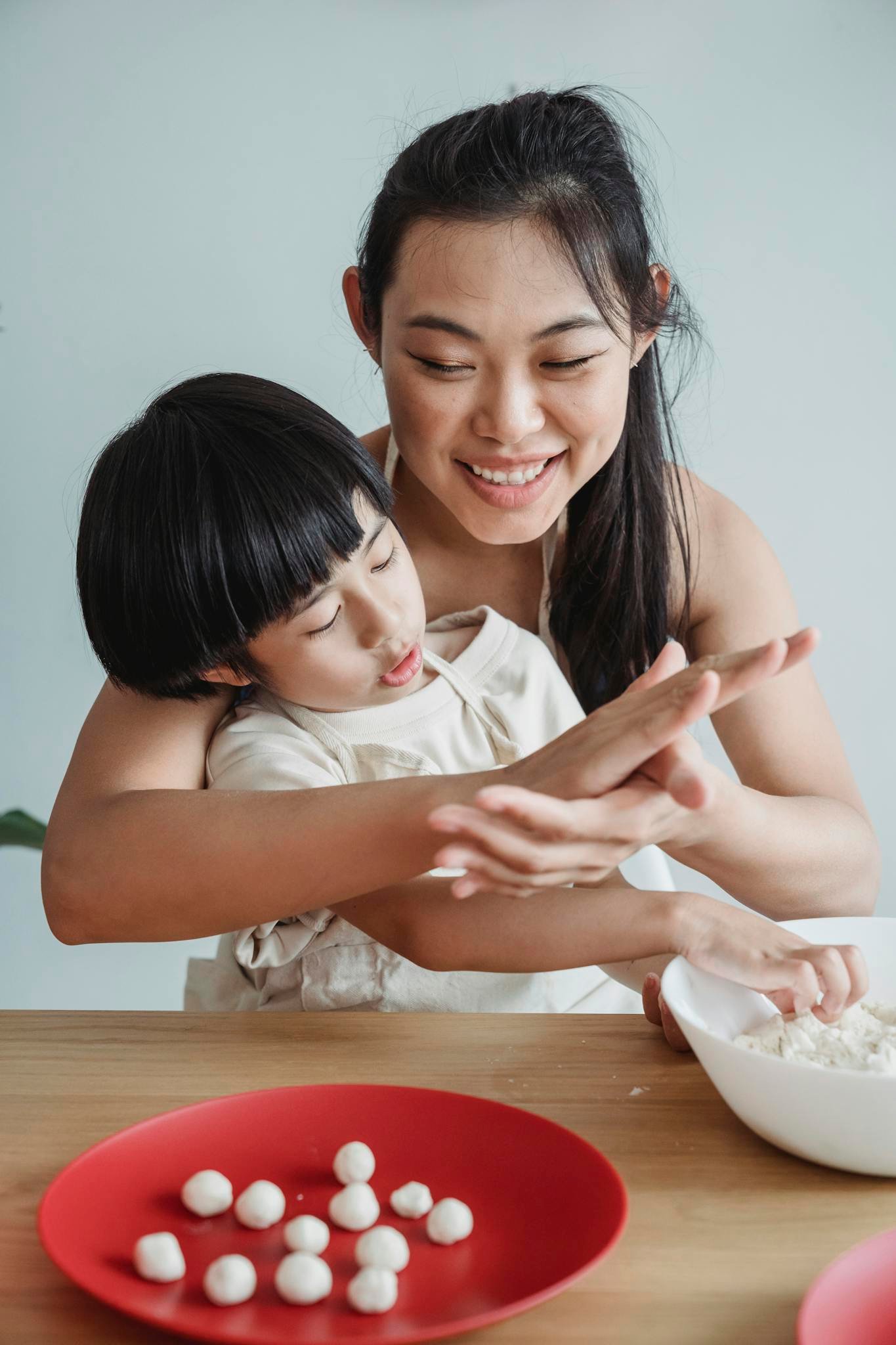 Mother teaching son to make dough. Smiling, they enjoy cooking together indoors.